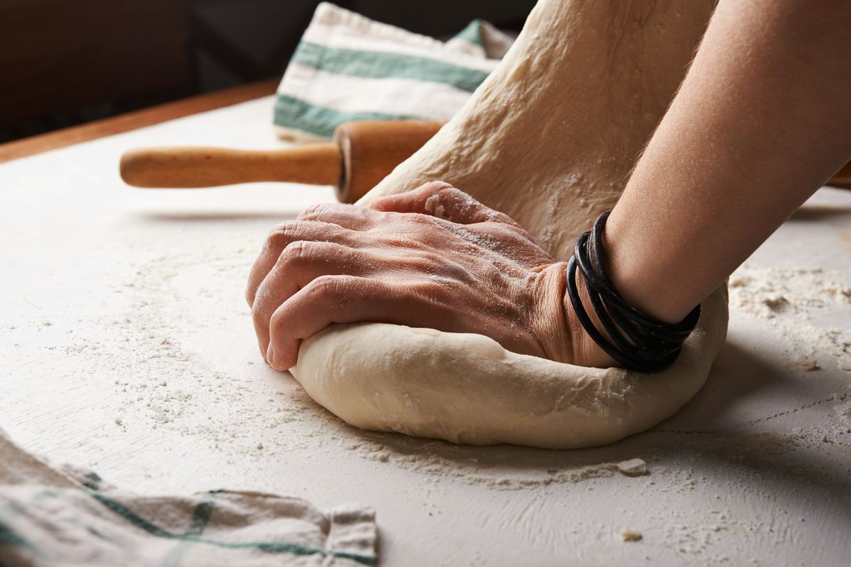 Handen kneden een bol deeg op een bebloemde werktafel